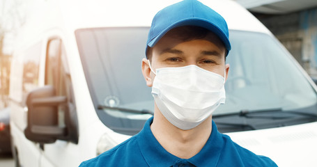 Fototapeta na wymiar Portrait of young courier in mask standing near delivery car
