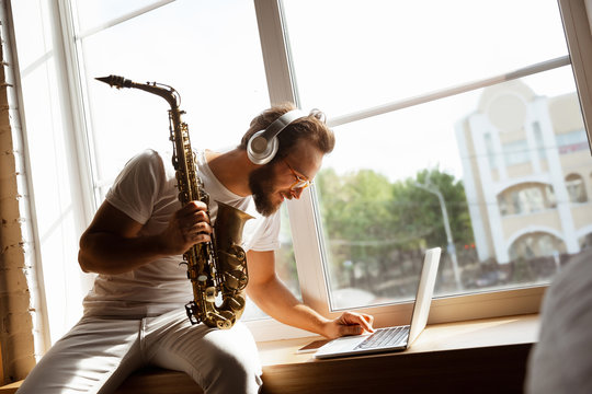 Caucasian musician playing saxophone during online concert at home isolated and quarantined. Using camera, laptop, streaming, recording courses. Concept of art, support, music, hobby, education.