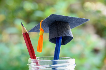 Global education success / graduate study aborad program concept : Black graduation cap or a mortarboard, blue and red pencils in a bottle, depicts achievement in higher mba learning course in academy - obrazy, fototapety, plakaty