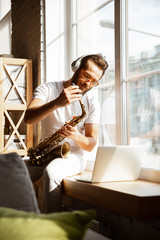 Caucasian musician playing saxophone during online concert at home isolated and quarantined. Using...