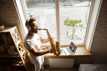 Caucasian musician playing saxophone during online concert at home isolated and quarantined. Using camera, laptop, streaming, recording courses. Concept of art, support, music, hobby, education.