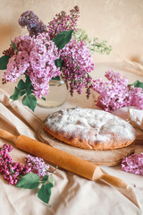 Fototapeta na wymiar Homemade Apple pie on a wooden table next to a bowl of lilacs. Gentle toning.