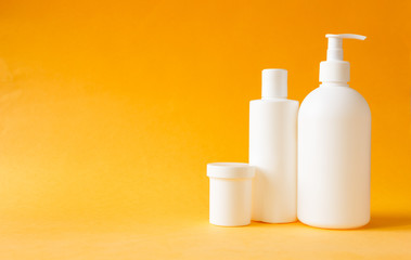 Cosmetics, moisturizer, three white plastic bottles with shower gel and shampoo on yellow background. Set of body and hair care products.