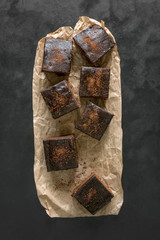 Freshly baked classic brownie on parchment are laid out on a black surface