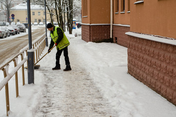 snow storm in the city. Roads and sidewalks covered with snow. Worker shovel clears snow. Bad...