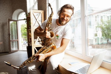 Caucasian musician playing saxophone during online concert at home isolated and quarantined. Using...