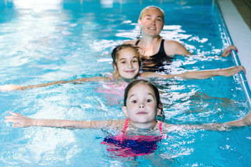 Mother with two daughters having fun in indoor swimming-pool. Girl is resting at the water park. Swimming school for small children. Concept friendly family sport summer vacation. Selective focus.
