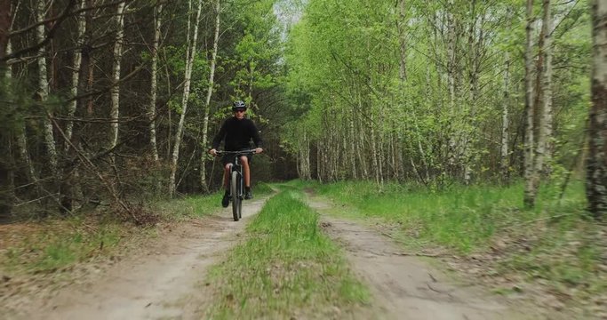 Young  man cyclist rides on a forest road. Teenager on a mountain bike rides through the forest. Man in a Bicycle helmet rides an mtb bike.