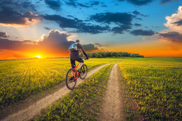 Ride of bike on a dirt road in a field at sunset.