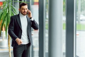 Young businessman standing in office hall and talking on phone