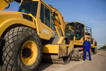 young man contractor builder in blue overalls is looking to the bulldozer wheel.