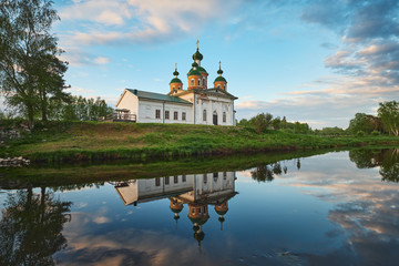 Summer landscape with the Orthodox Church and the reflection of clouds in the water of the river.