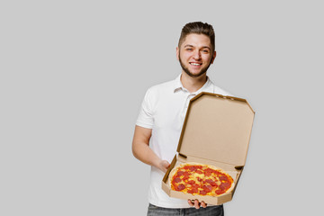Online pizza safety delivery servise from restaurant. Pizza with cheese boards advertise. Isolated white background with empty space for advertise. Young caucasian courier man shows pizza and smile