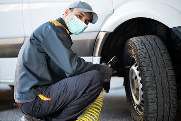 Masked mechanic checking the pressure of a van tire