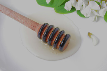 
honey dipper with liquid honey on a background of green flowers.