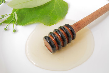 
honey dipper with liquid honey on a background of green flowers.