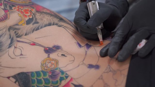 A close-up video of a tattoo artist. He is making a Japanese tattoo on a man's back. A high resolution as 4K.