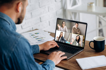 Work online by a video conference with colleagues. A man in a stylish wear sits at his workplace at home and solves working issues on video communication with business partners