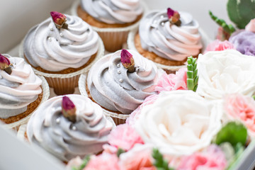 closeup of delicious sweet muffins with pink-gray butter cream in a box with flowers