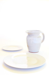 White chefs plates with white handmade pottery pitcher on white backgroun