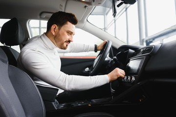 Handsome bearded businessman is sitting in a new car in car dealership