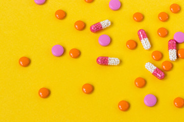 Multi-colored pills are scattered on a bright yellow background, top view. Medication for the disease for patients. Dose drugs and vitamins for health. Copy space. Close up.