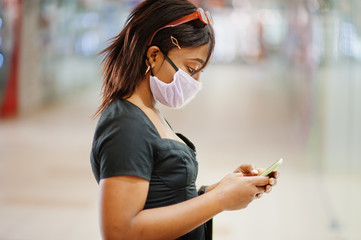 African american woman wearing face protective medical mask for protection from virus disease with mobile phone in mall during coronavirus pandemia.