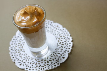 One glass with a Dalgona coffee cocktail, front view. Trendy Korean quarantine drink on a brown. 