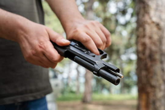 Close up on gun in hands of unknown caucasian man holding and cocking the black gun load or unload while standing in the woods in nature sunny summer day side view