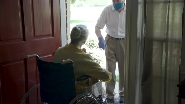 A church volunteer wearing a mask brings food to an elderly woman in a wheelchair that may otherwise be unable to get groceries during COVID19 .