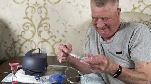 Elderly man fills an inhaler nebulizer with medication from a syringe. Theme of a serious and incurable disease of lungs and respiratory system. Procedures for patients with COPD and lung diseases.