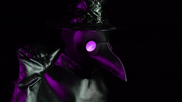 Man in plague doctor costume with crow-like mask showing bye-bye gesture isolated on black background. Creepy mask, historical costume concept. Epidemic