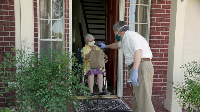 A church volunteer wearing a mask brings food to an elderly woman in a wheelchair during COVID19.