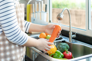 Asian healthy woman washing an carrot and other fvegetable above kitchen sink and cleaning a fruit / vegetable with water to eliminate the chances of contamination COVID-19..
