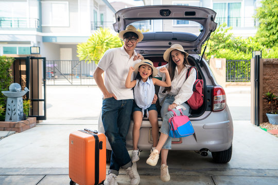 Portrait Of Asian Family With Father, Mother And Daughter Looks Happy While Preparing Suitcase Into A Car For Holiday. Shot In The House Garage..