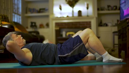 A mature man follows an fitness instructor on TV in a virtual workout because his gym remains closed due to the COVID19 pandemic.