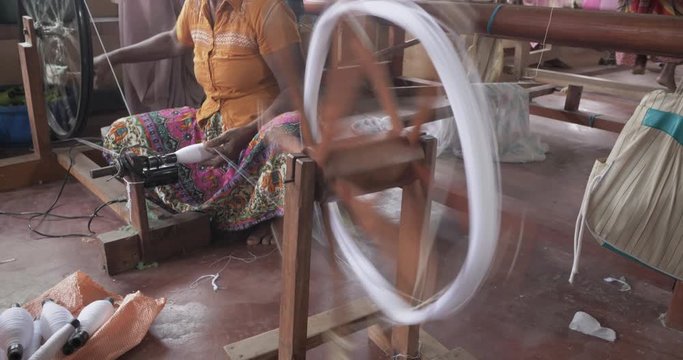 Hands of an old woman using an old spinning wheel to turn wool into yarn