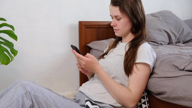 Pretty pregnant woman sitting on floor at home or hotel using modern smartphone touching screen, cute future mother use phone to view messages or correspond with friends online. Social distance
