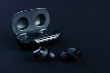 Earbud headphones side profile - displayed in front of opened black wireless earbud charging case on black background