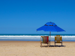 Two beach recliners and blue umbrella in front of the sea in a sunny day. Geribá beach, Buzios, Brazil