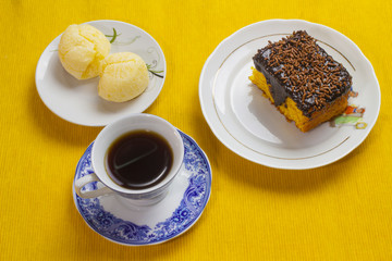 Carrot cake icing chocolate, Brazilian cheese bread and coffee cup and on the yellow placemat.