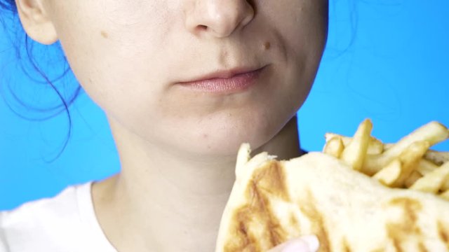 closeup of young woman eating gyro isolated on blue background