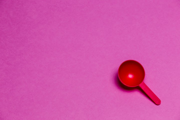 Red Plastic Round Spoon Placed Over Colorful Pink Background.