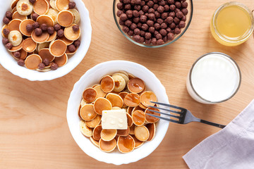 Pancake cereal - food trend coronavirus quarantine. Breakfast with tiny pancakes, cocoa crispy balls, milk and honey on wooden table. Funny food for kids, mini pancakes.