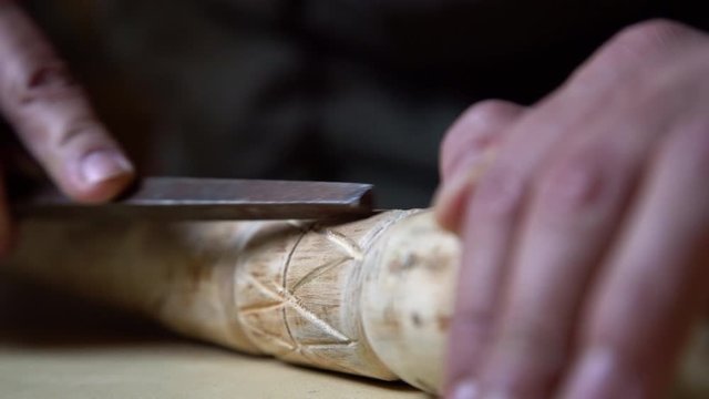 Close up process of man making wooden walking stick indoors during quarantine. Carving wood stick on the table using knife