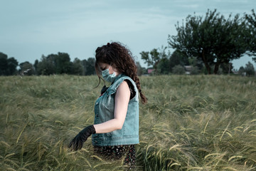 young woman wearing a surgical mask  and gloves is walking in a field of wheat 