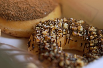 Selective focus of donuts, glazed with melted chocolate and decorated with almond and nuts, lie on a platter.