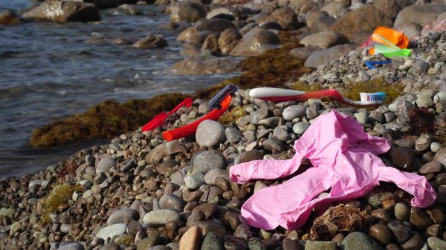 Old used discarded latex glove, toothbrush, disposable razor in a seashore. Garbage in nature, environment. Plastic that are being dumped into oceans. Environmental and water pollution