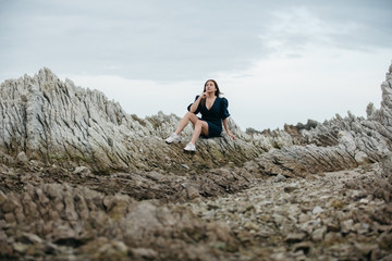 Naklejka premium Portrait of young asian woman on stones near sea. Beautiful girl is resting on coast, enjoying outdoor recreation at Kaikoura, New zealand.