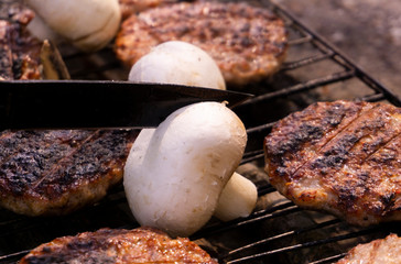 Beef BBQ Cooking of burger meat and mushroom. Iron barbeque grill pan with fire and food. Hamburgers outdoors barbecuing on coals. Closeup beef for burgers on cast iron grill. Juicy fat food grilled.